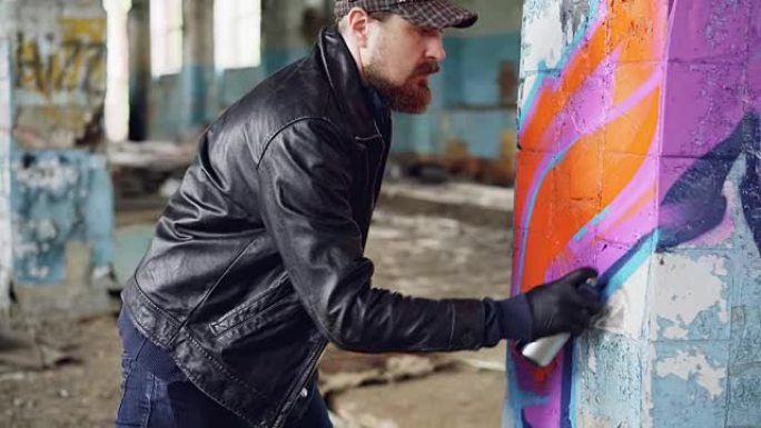 Handosme man涂鸦艺术家专注于旧空房子中柱子上的气溶胶涂料的绘画线条。废弃建筑、墙面艺术和