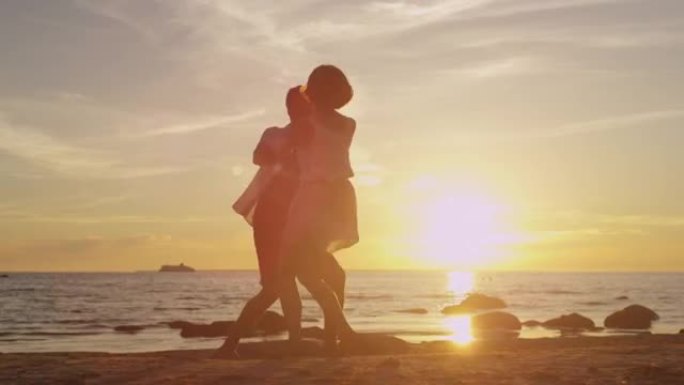 女孩和男人一起在海滩上玩得开心。在日落时分牵手旋转。