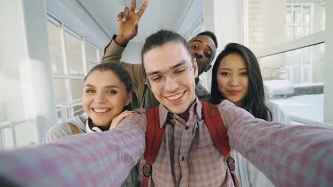 四个积极开朗有吸引力的多民族朋友的观点拿着智能手机聊天自拍照片，站在大学走廊里玩得开心