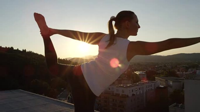 特写: 强大的女孩在日落时在屋顶上做舞蹈瑜伽的姿势