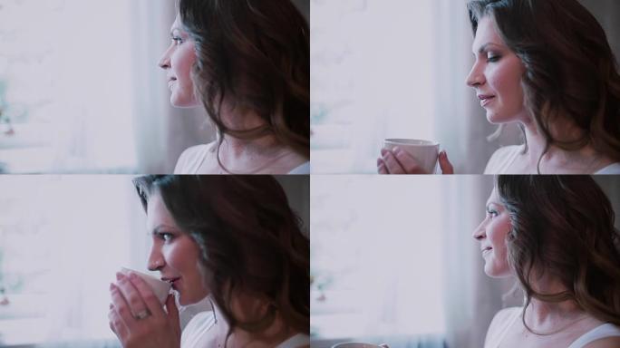 年轻美女坐在窗前喝咖啡的肖像。女孩微笑着，在家吃早餐