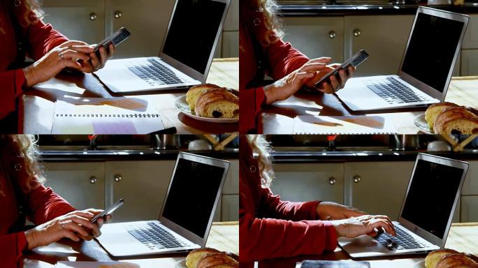 成熟的女人在家里的厨房里使用笔记本电脑和手机4k
