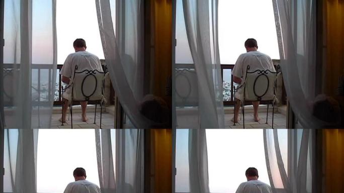 在窗帘后面工作。男子在阳台/露台上使用笔记本电脑