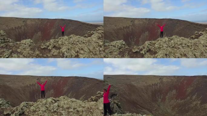 空中: 年轻女子在火山口上方举起手臂