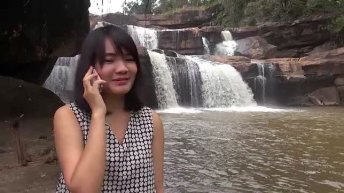 迷人的女人在美丽的瀑布旁用手机聊天