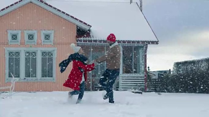 年轻美丽的夫妇在飘落的雪中跳舞和旋转。快乐的男人和女人在他们田园诗般的房子的院子里玩得开心。