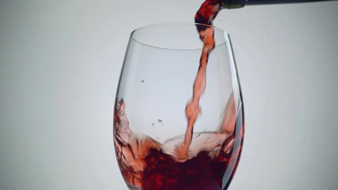 将红酒倒入白色背景的玻璃杯中。慢动作