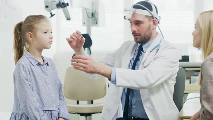 友好的耳鼻喉科儿科医生检查一个微笑的小女孩的耳朵。使用专用手电筒设备进行儿童健康检查。母亲带着一个小