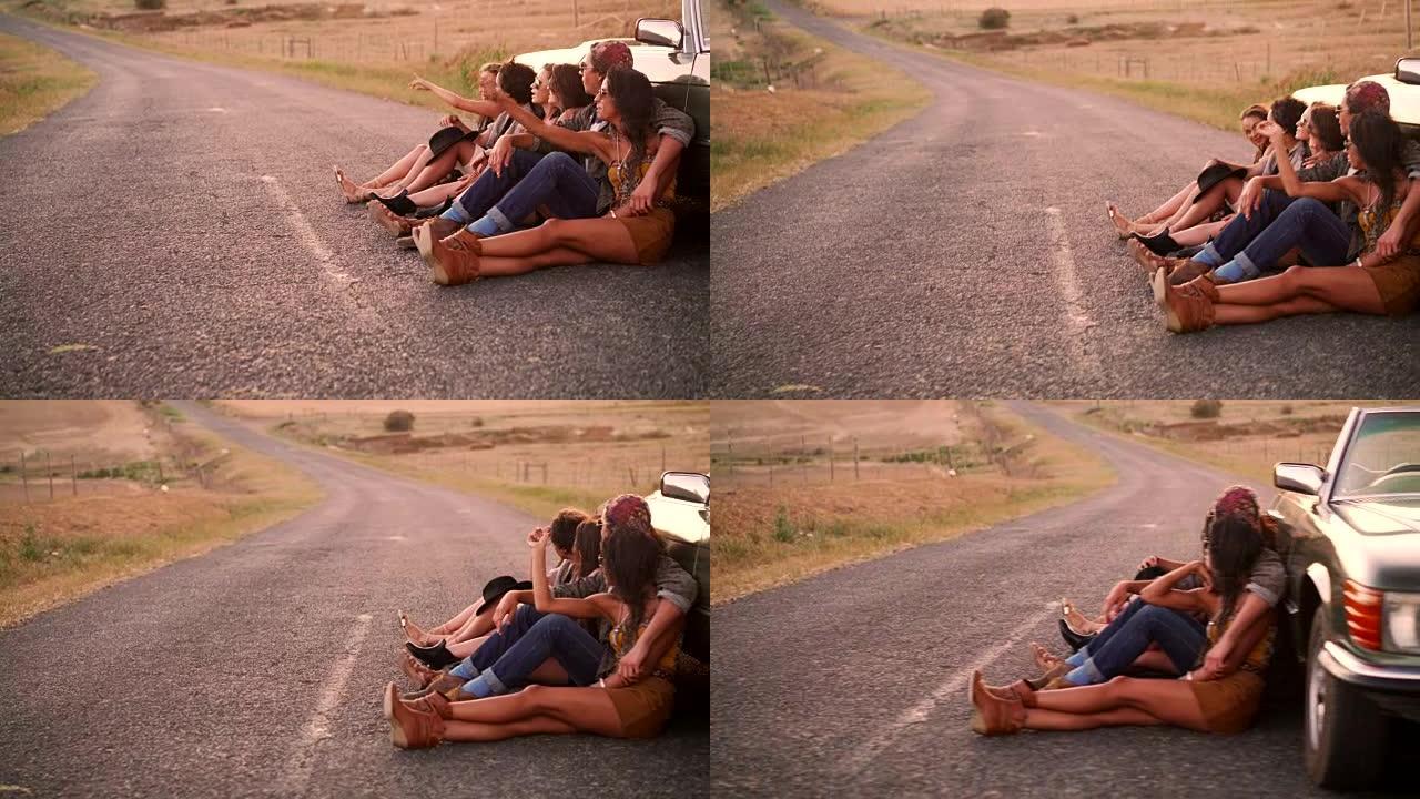 波西米亚风格的朋友靠在公路上的老式敞篷车上休息