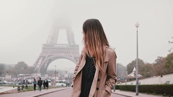 年轻迷人的女人走在法国巴黎埃菲尔铁塔附近。快乐的女孩环顾四周，微笑着。慢动作