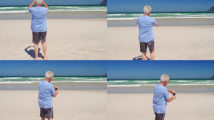 高级男子在海滩用手机拍照