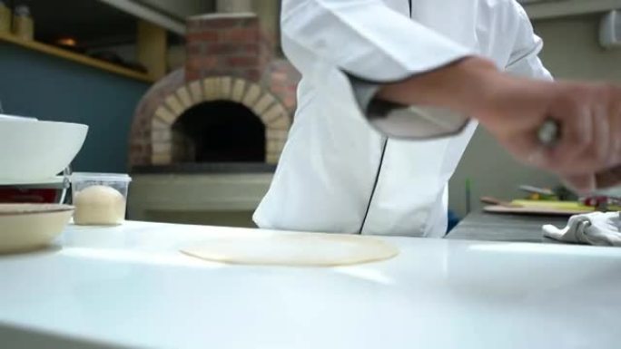 意大利厨师在一家餐厅做披萨，并在面团上撒上面粉，同时使用金属rolling面带微笑