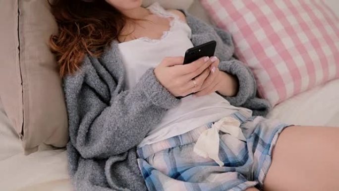使用无线技术的年轻女子躺在床上在家聊天。智能手机上的女孩类型使用触摸屏