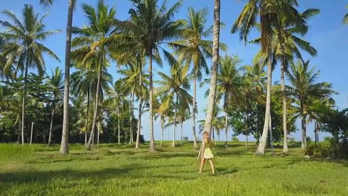 特写: 迷人的年轻女子在郁郁葱葱的棕榈树之间的草地上行走