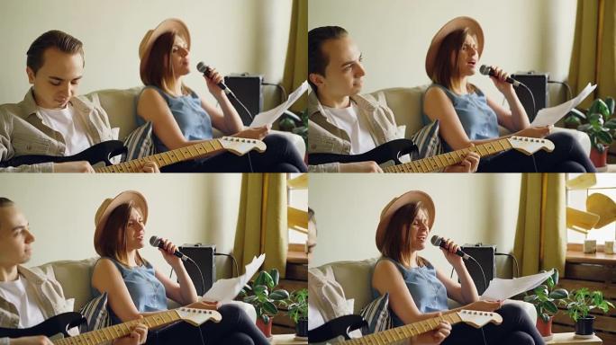 创意音乐二重唱在家里练习女人在麦克风里唱歌，男人在弹吉他。年轻开朗的人穿着便装。