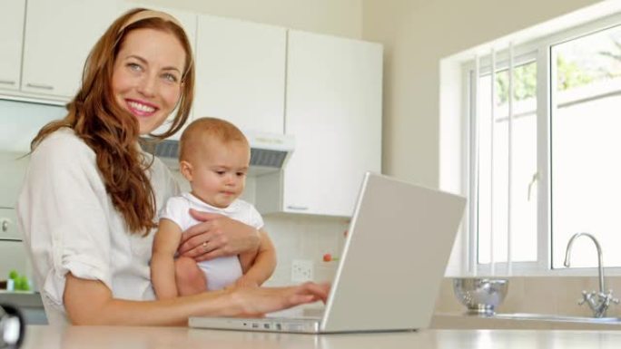 美丽的黑发女人用笔记本电脑抱着她的小女儿