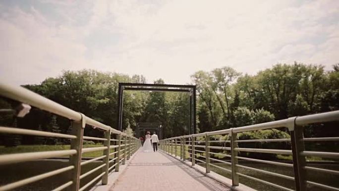 刚刚结婚。夏天穿着婚纱的新娘和新郎在桥上牵手行走的背景图