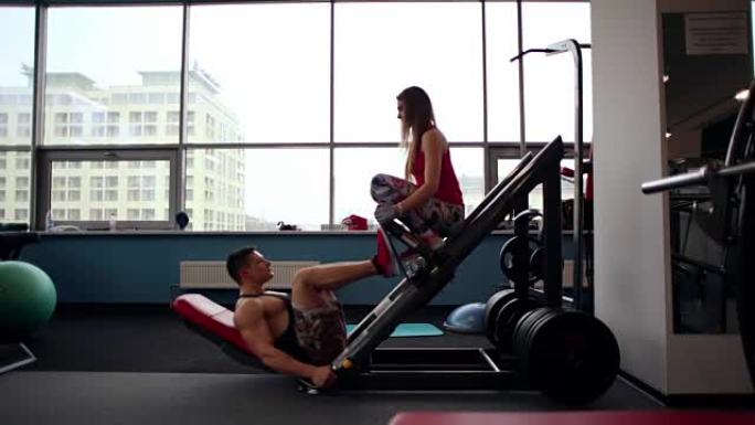 一名男运动员在健身房锻炼腿部按压运动的侧面图。坐在媒体上的运动女人