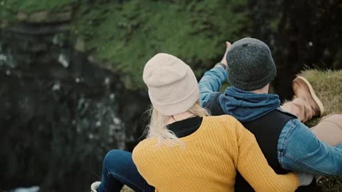 年轻夫妇坐在悬崖边休息的后景。享受美景的旅游男女