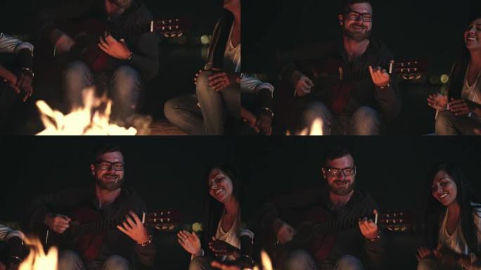快乐的男人在篝火晚会为朋友弹吉他