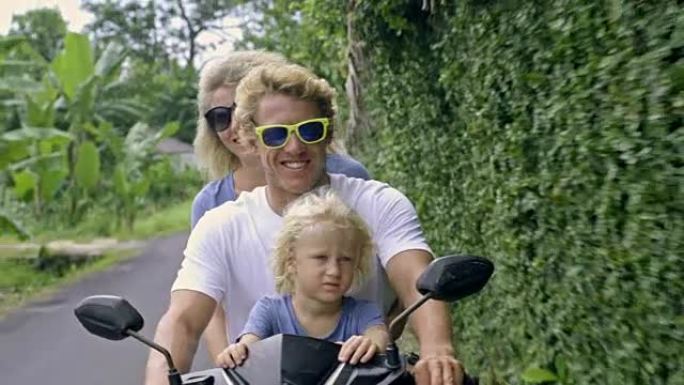 无忧无虑的家庭骑在热带地区的踏板车上