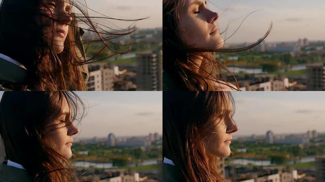 风吹起长长的黑发。站在屋顶上的女孩拉直头发，看着城市。特写。慢动作