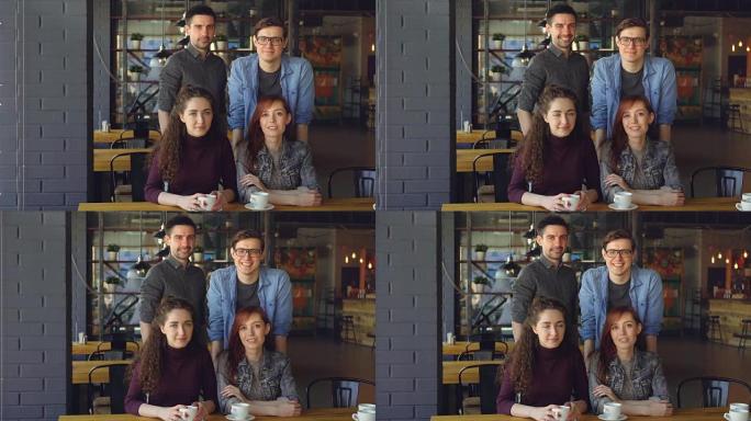 两对夫妇的肖像穿着休闲服装的快乐年轻人朋友在现代咖啡馆里，茶杯微笑着看着相机。外出就餐和友谊概念。