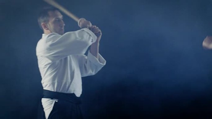 武术大师教他的年轻学生如何用木剑博肯战斗。争吵在几秒钟内结束，大师获胜。拍摄是在黑色背景和慢动作中隔