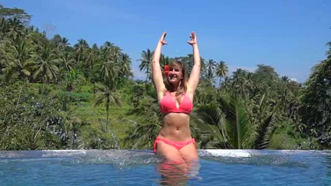 特写欢快的女孩在热带岛屿的无边泳池里溅水滴