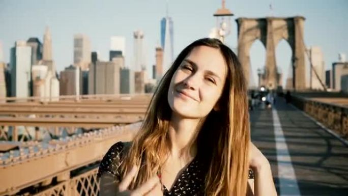 年轻的欧洲美丽的旅行者女孩抚摸头发，看着相机，在纽约布鲁克林大桥微笑4K
