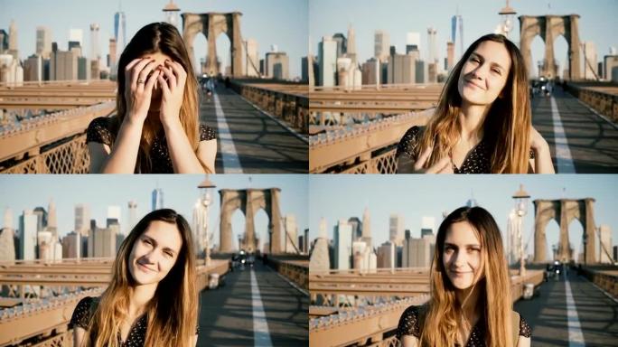 年轻的欧洲美丽的旅行者女孩抚摸头发，看着相机，在纽约布鲁克林大桥微笑4K