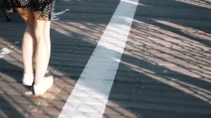 摄像机跟随女性的双腿沿着沥青和带有条纹的木制道路行走，上面覆盖着美丽的细阴影4K
