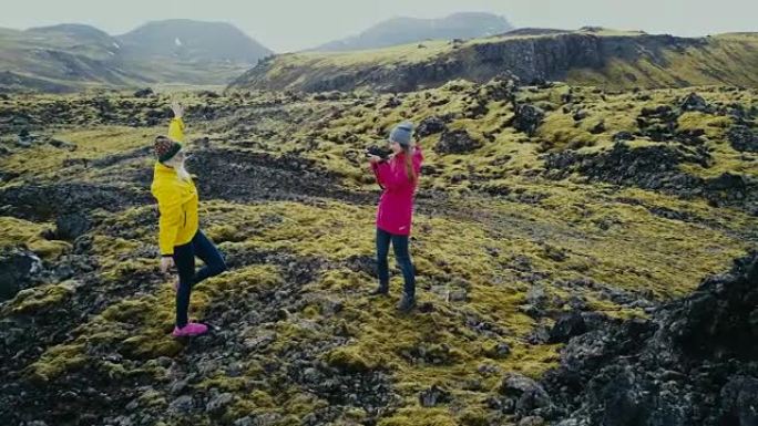 一架直升机飞近了在冰岛熔岩上拍摄照片的两名女子。游客在山上拍照