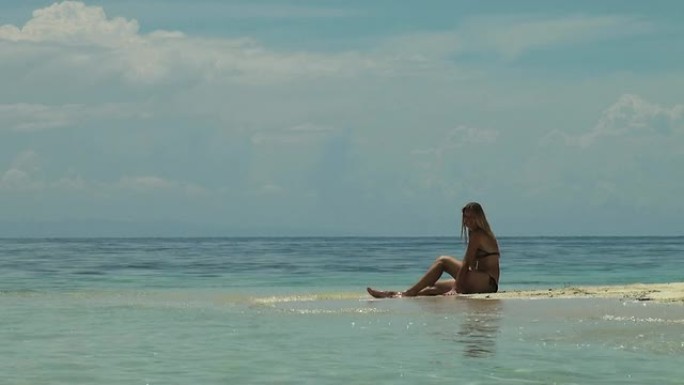 一个微笑的女人坐在海洋中的沙嘴上