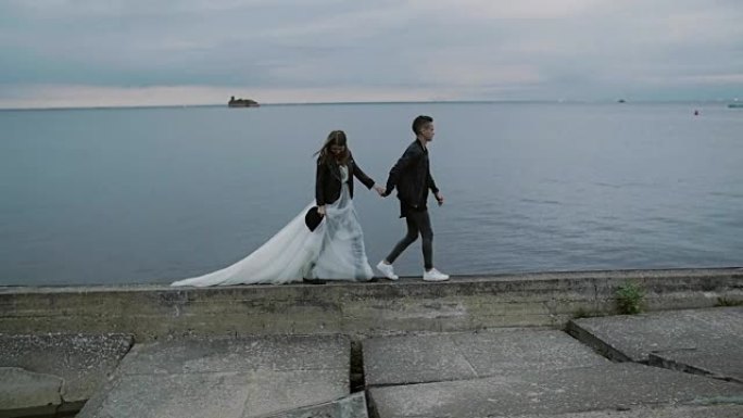 美丽时尚的情侣新娘和新郎在黄昏时沿着堤岸行走，慢动作