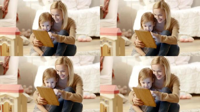 美丽的妈妈和她的小女儿在平板电脑上阅读儿童书籍很开心。儿童房里摆满了玩具。