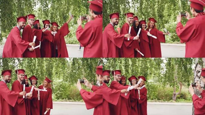 顽皮的年轻人毕业生正在摆姿势拍照，制作有趣的姿势和手势，而他们的朋友正在使用智能手机相机拍摄它们。