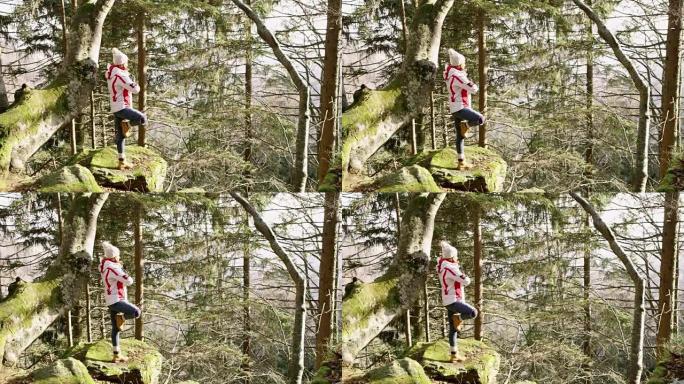 4k年轻女子在阳光森林的岩石上练习瑜伽树姿势，实时