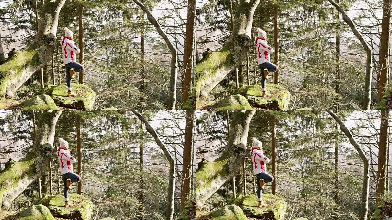 4k年轻女子在阳光森林的岩石上练习瑜伽树姿势，实时