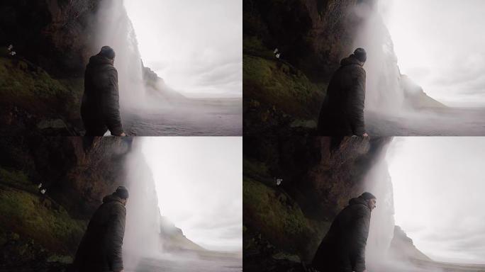 男子在gopro相机上拍摄冰岛美丽而强大的Seljalandsfoss瀑布。水溅到岩石上