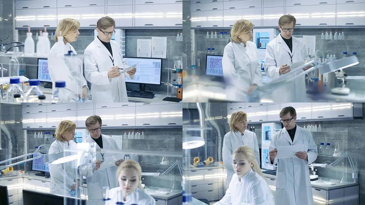 女性和男性首席科学家走过现代实验室，讨论未来的可能性。年轻的女助理在她的办公桌前工作。