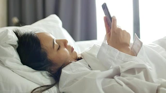 亚洲妇女早上醒来后在床上使用社交媒体