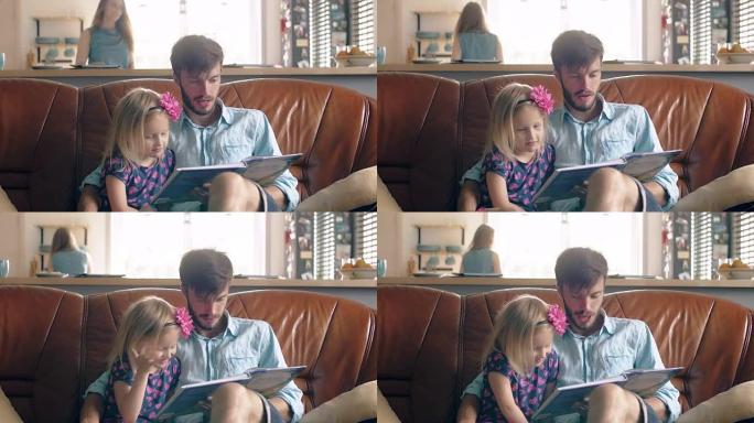 幸福的家庭。年轻的父亲和他的金发小女儿正在餐厅的皮沙发上读一个故事。全高清