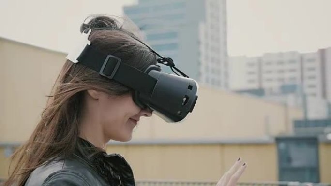 挥舞着头发的黑发女孩在屋顶上使用3D虚拟现实耳机。全高清