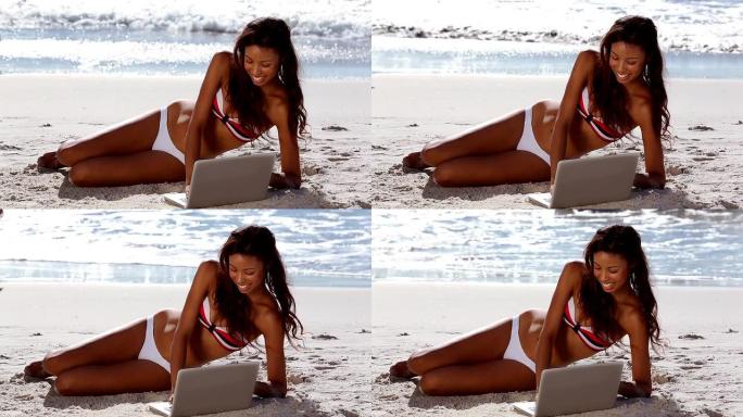 迷人的女人在海滩上用笔记本电脑放松