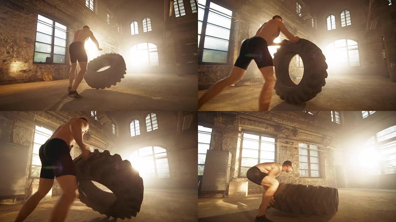 强壮肌肉的男人举起轮胎作为他的健身计划的一部分。他满身是汗，在一个废弃工厂改造成的健身房锻炼。