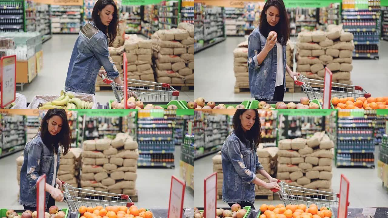 迷人的女孩快乐的顾客正在超市选择水果，购买香蕉，苹果和橙子，并将它们放入购物车。健康的生活方式和商店