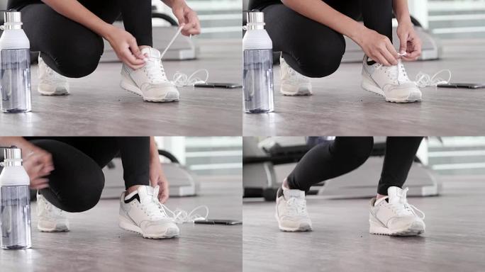 女跑步者的脚特写镜头准备用瓶装水、耳机和电话系跑鞋，以激发室内健身房运动跑道上有氧运动训练的音乐动机