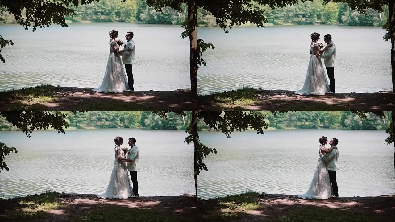 一对结婚那天接吻的夫妇的侧视图。快乐的新娘和新郎在河岸上美丽的地方