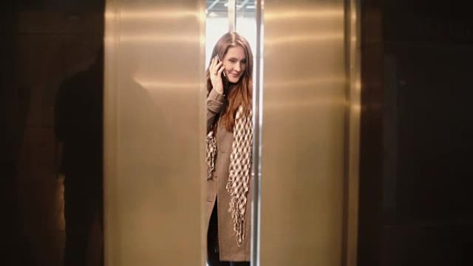 女人站在电梯里，用智能手机聊天。女性按下按钮，门关闭